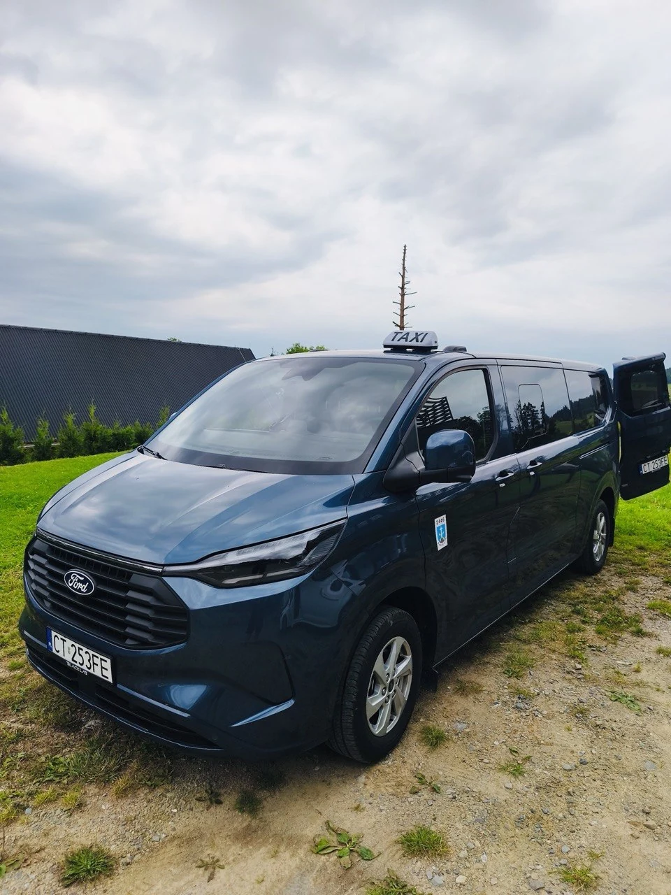 Синий микроавтобус Ford с табличкой TAXI, вид спереди