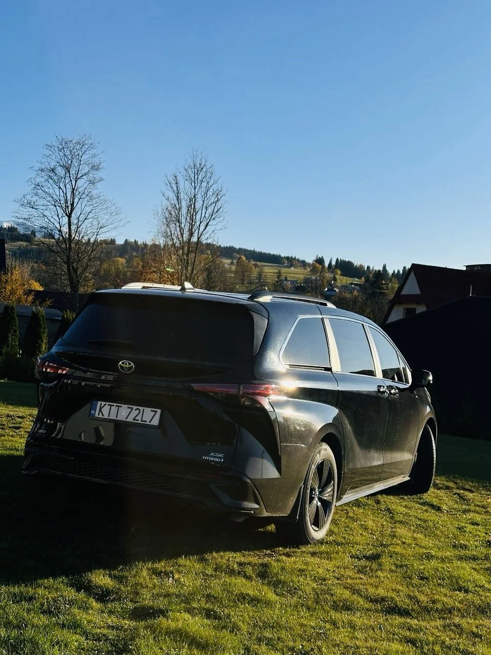 Чёрная Toyota Sienna на фоне зелени, вид сзади